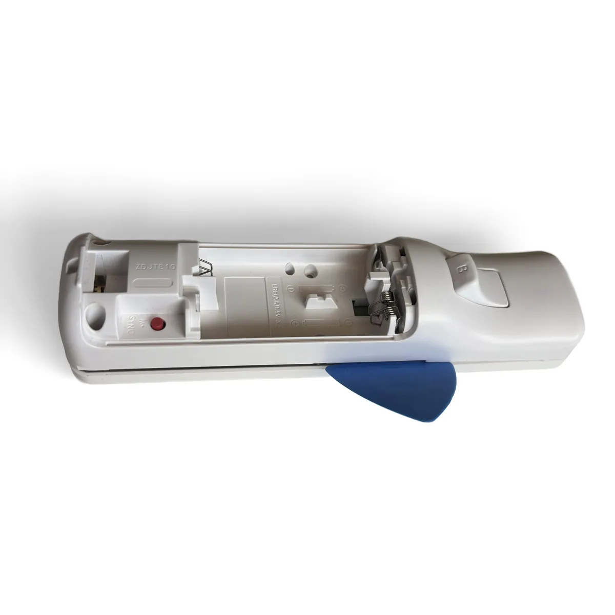 Blue opening pick pushed into the seam near the battery bay, with an arrow pointing along the seam toward the trigger end